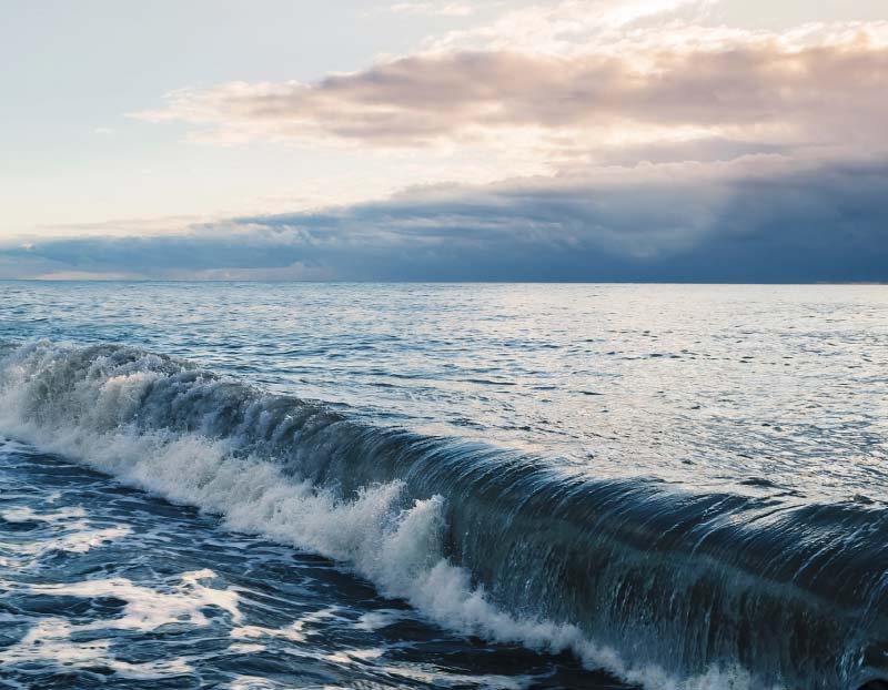 alm ocean wave curling and breaking near the shore under a soft twilight sky